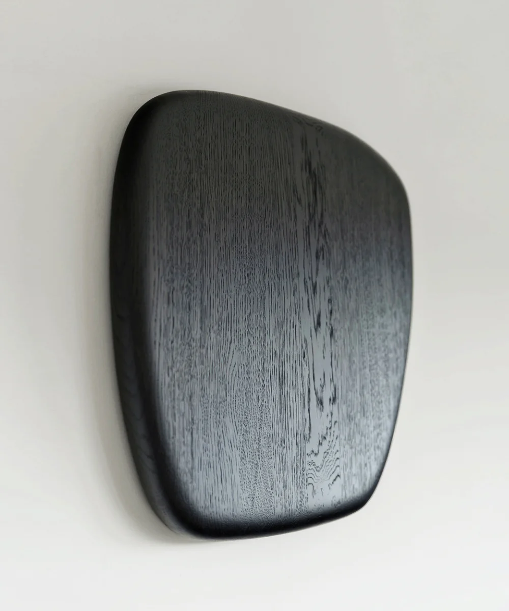 Minimalist wooden sculpture in dark chocolate black tones, featuring smooth, rounded organic shapes