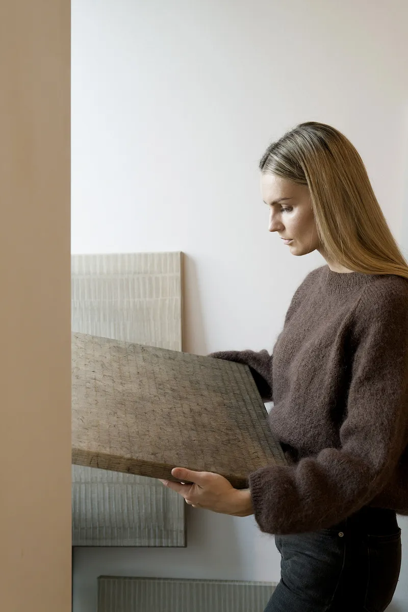 Marta Rószczka, contemporary Polish artist, holding abstract painting from her Concordia series in her art studio.